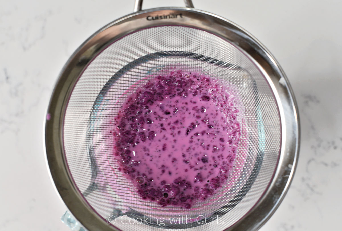 Pink Panna Cotta mixture in a strainer over a measuring cup. 