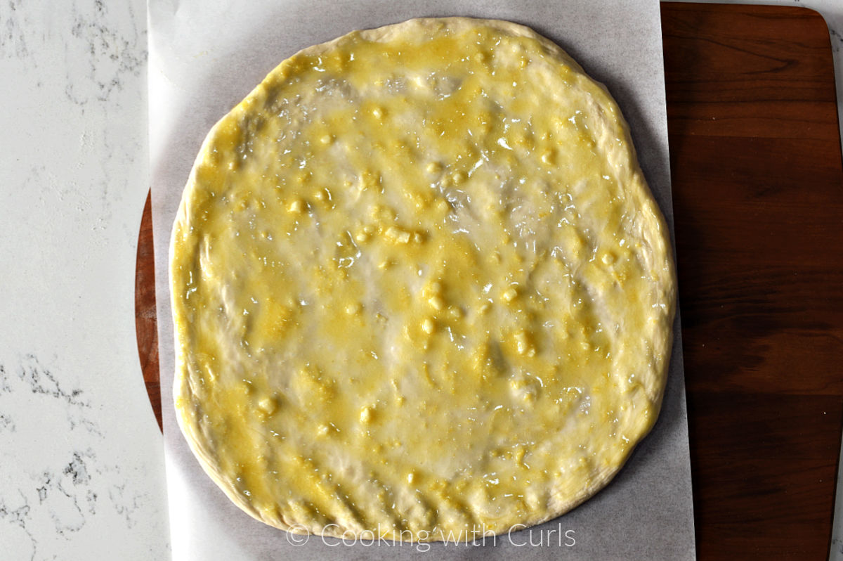 Pizza dough circle on parchment paper topped with garlic lemon sauce. 