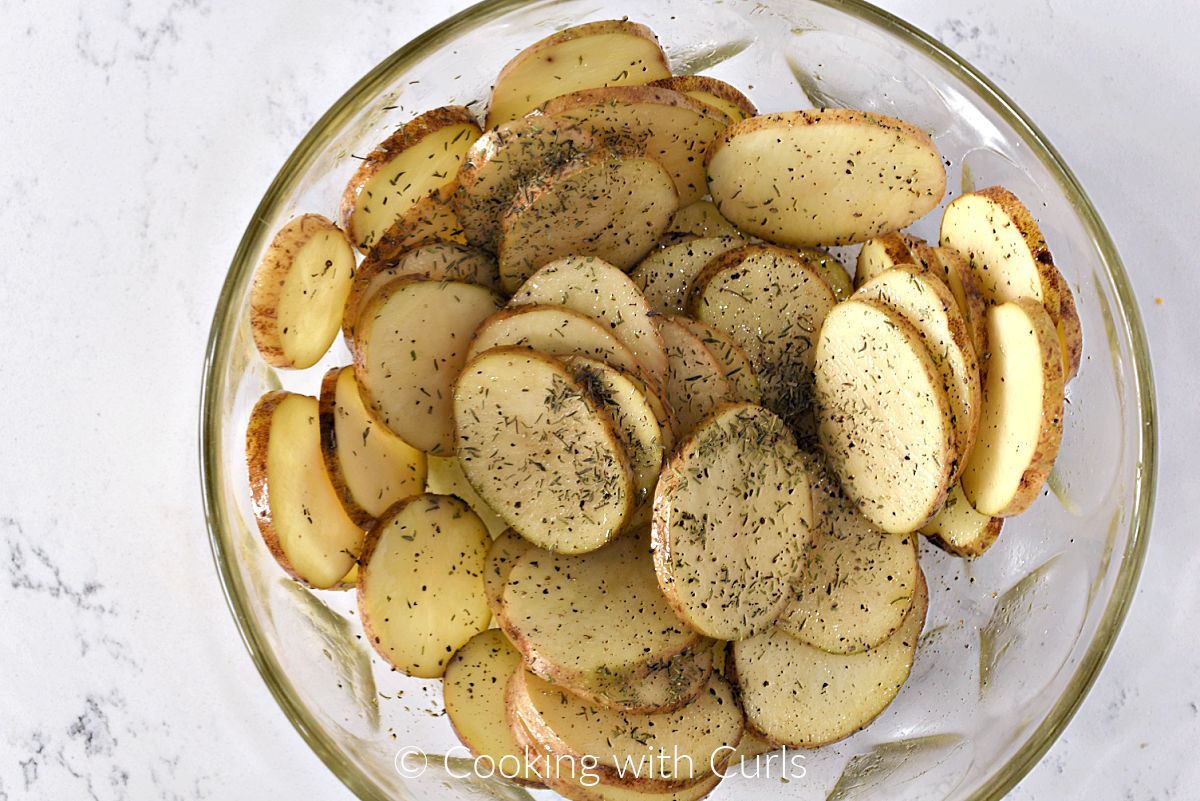 Potato slices tossed with oil and herbs in a large bowl. 