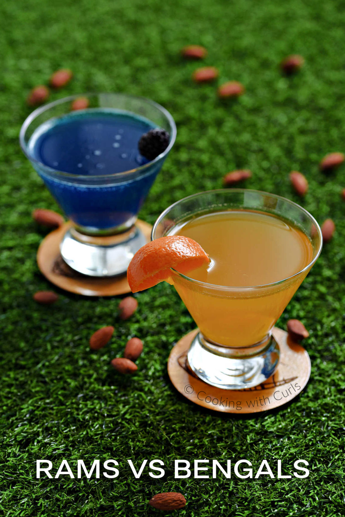 One blue and one orange martini in short glasses on green grass.