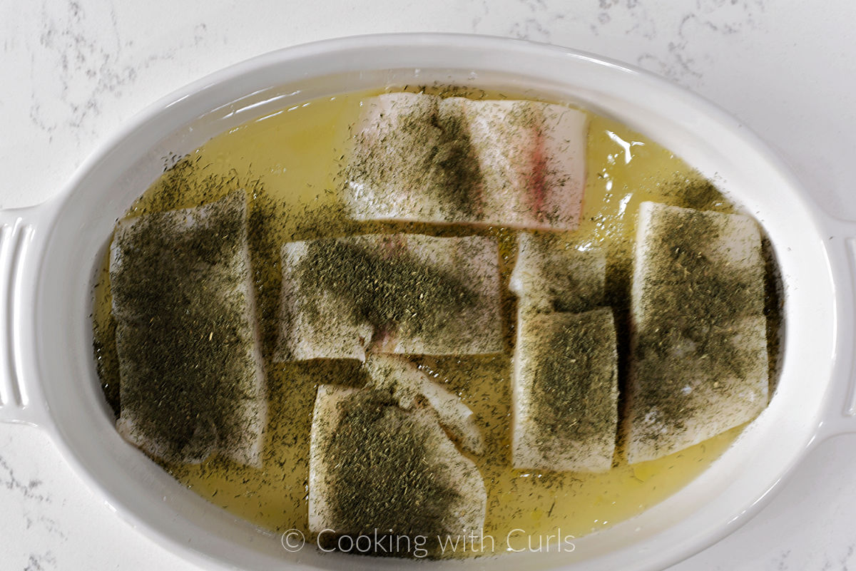 Six cod filets in a baking dish covered with white wine and dried dill. 