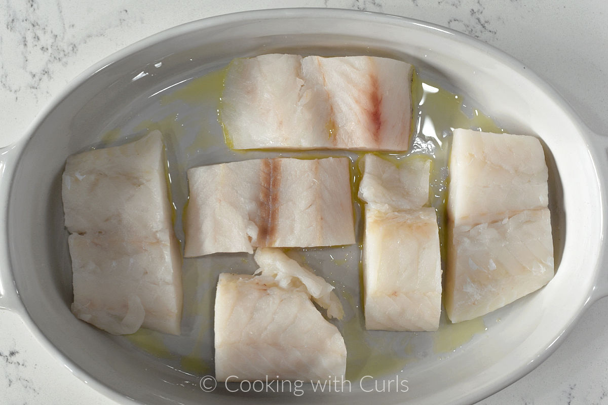 Six cod filets in a baking dish with olive oil. 