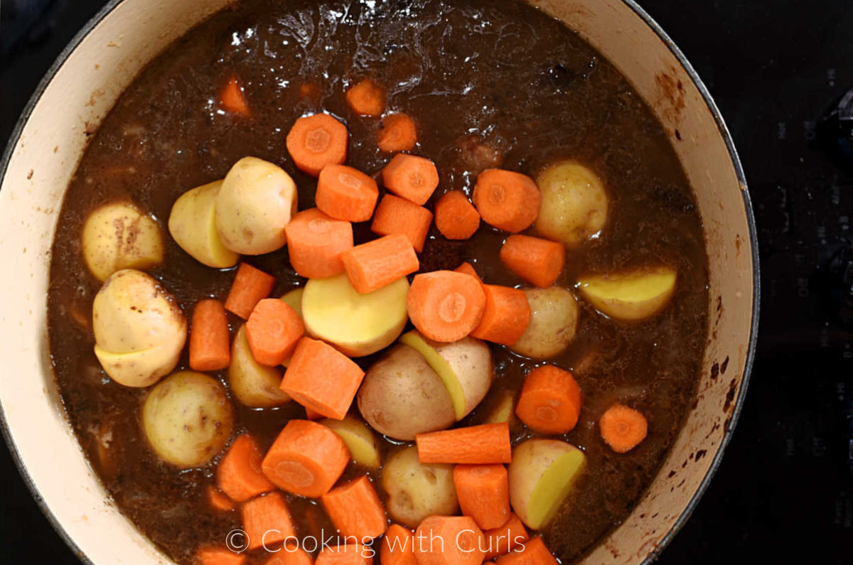 Sliced carrots, halved potatoes and beef chuck roast in Guinness gravy inside a Dutch oven. 