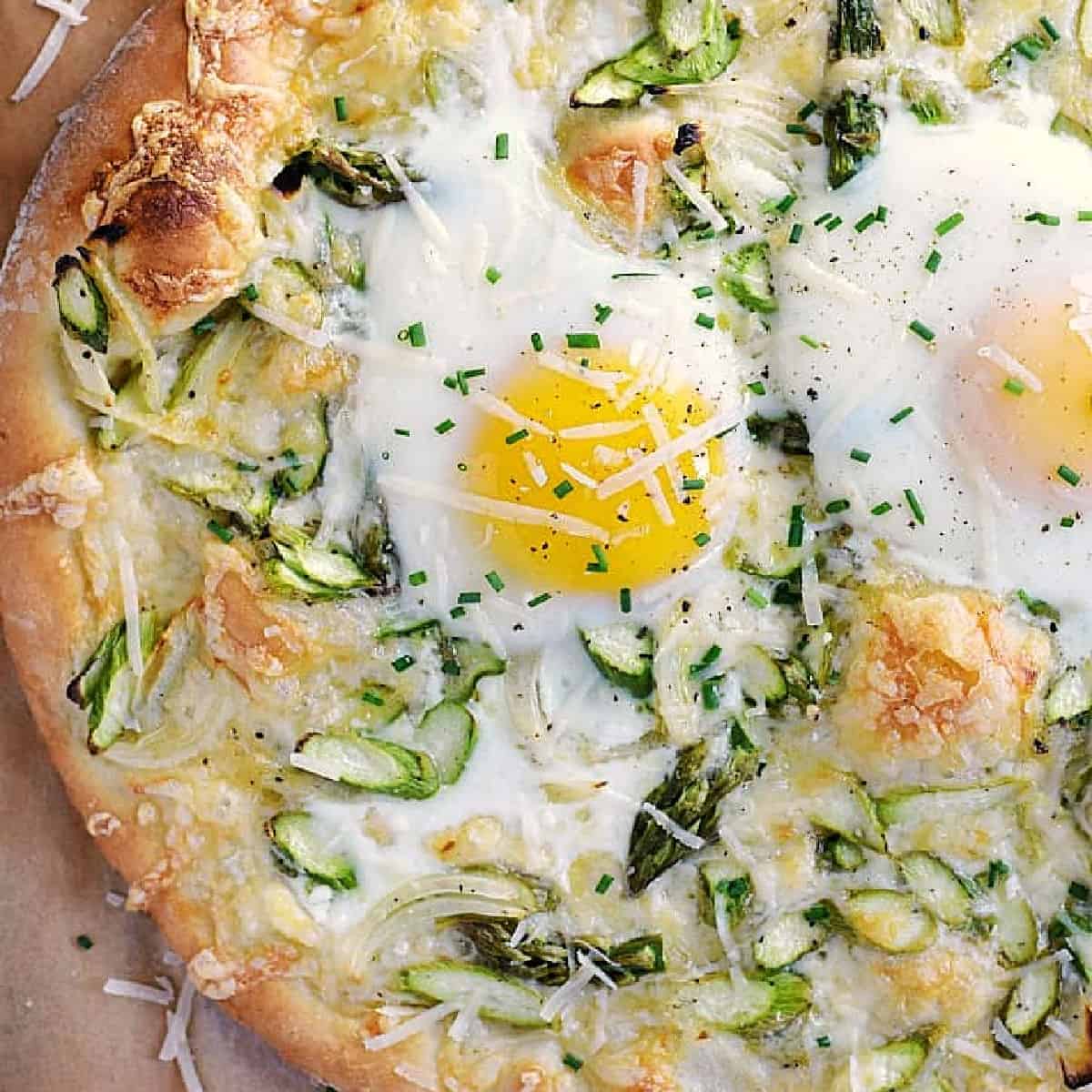 Pizza crust topped with asparagus, shredded cheese, and sunny side up eggs.