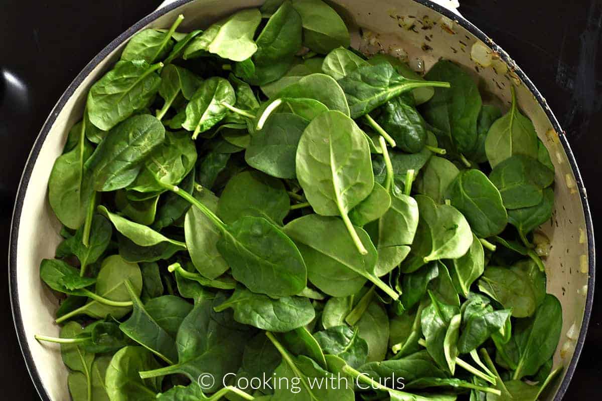 Baby spinach leaves added to the onion mixture in a skillet. 