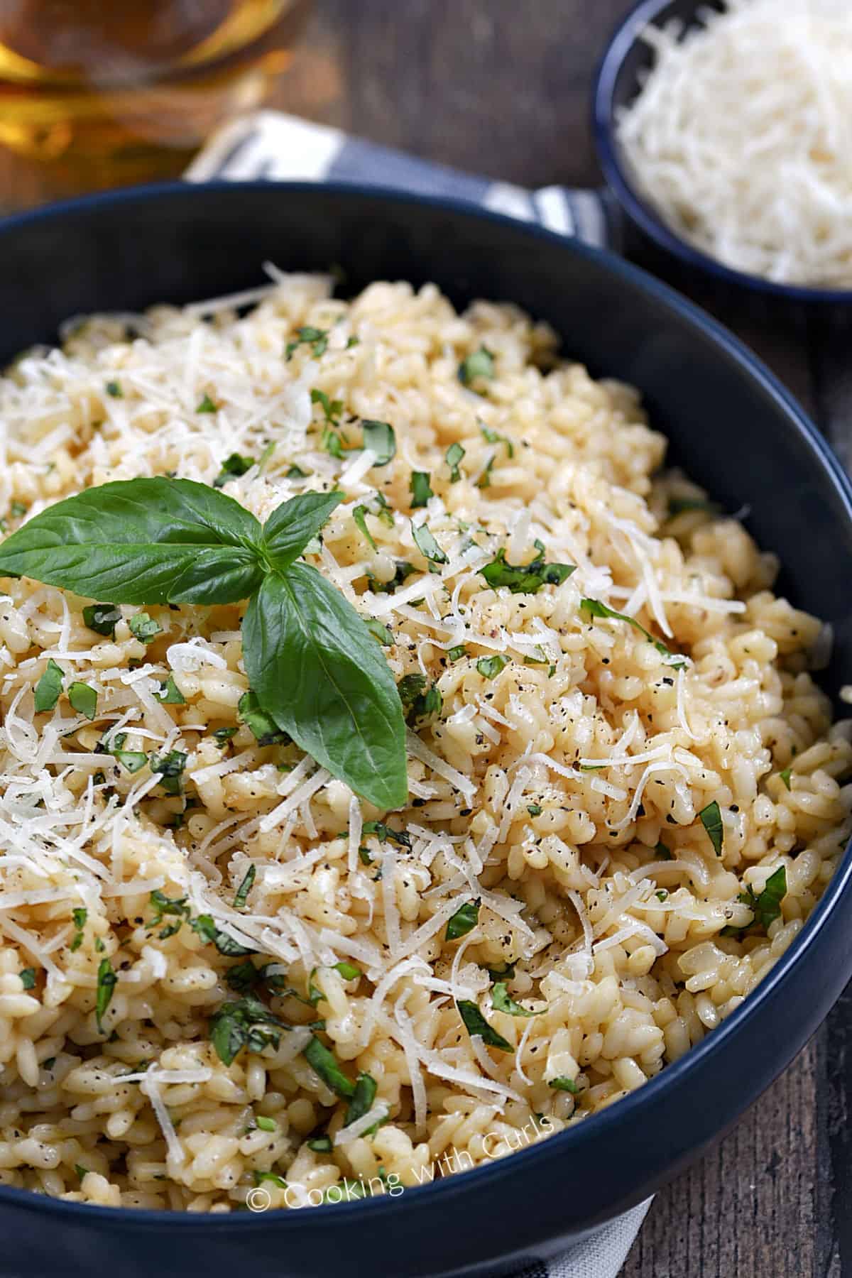A close-up image of a large bowl filled with basil risotto topped with fresh basil leaves and grated parmesan cheese.