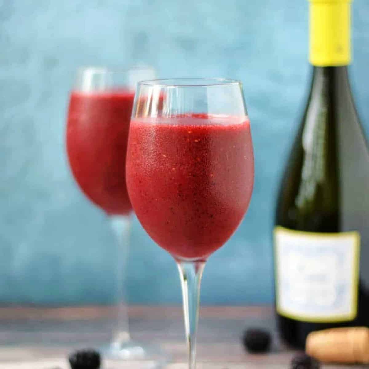Two wine glasses filled with blended wine and frozen berries.
