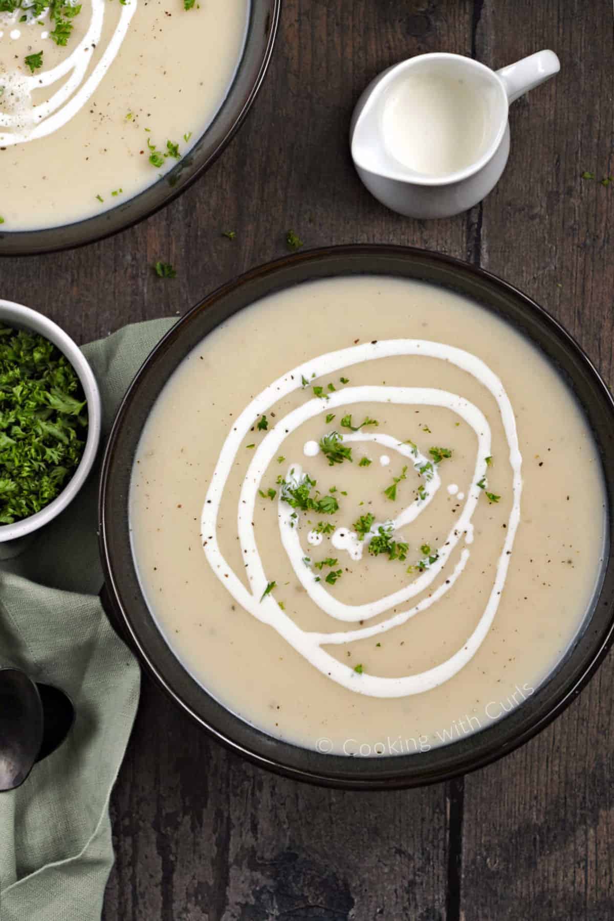 Looking down on two bowls of Irish Potato Leek Soup drizzled with cream and sprinkled with minced parsley. 