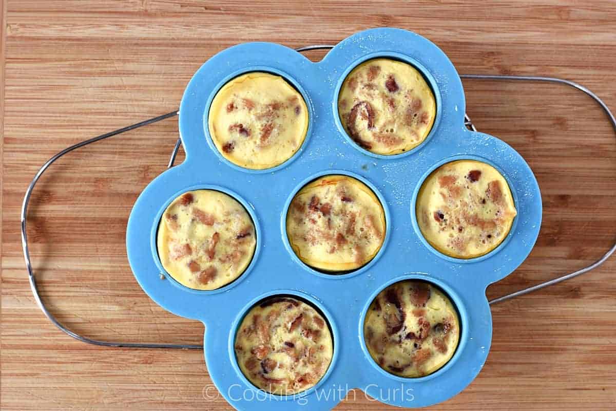 Cooked egg bites in a silicone mold sitting on a metal trivet on a bamboo cutting board. 