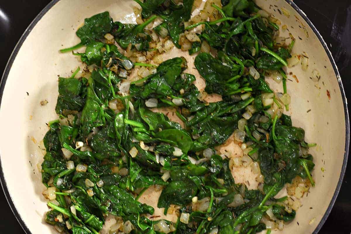 Cooked spinach leaves and diced onion in a skillet. 