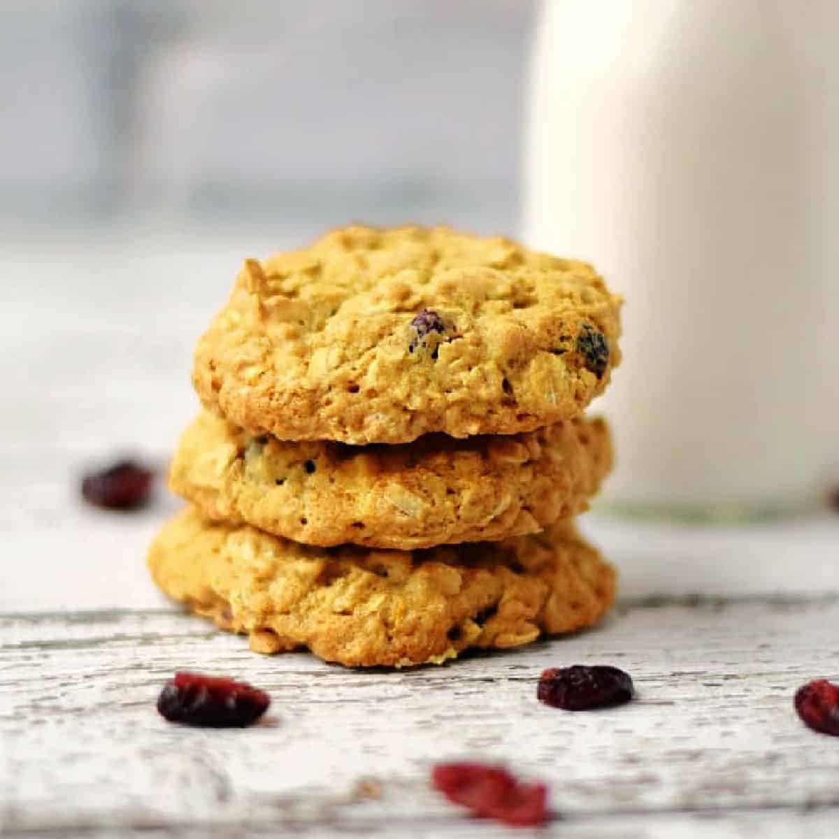 A stack of three cranberry white chocolate oatmeal cookies in front of a glass of milk.