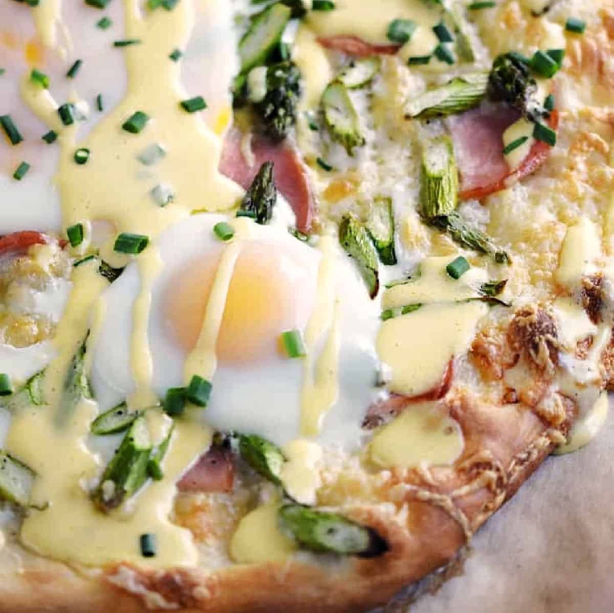 Pizza topped with sunny side up eggs, ham, asparagus, hollandaise sauce and chives.