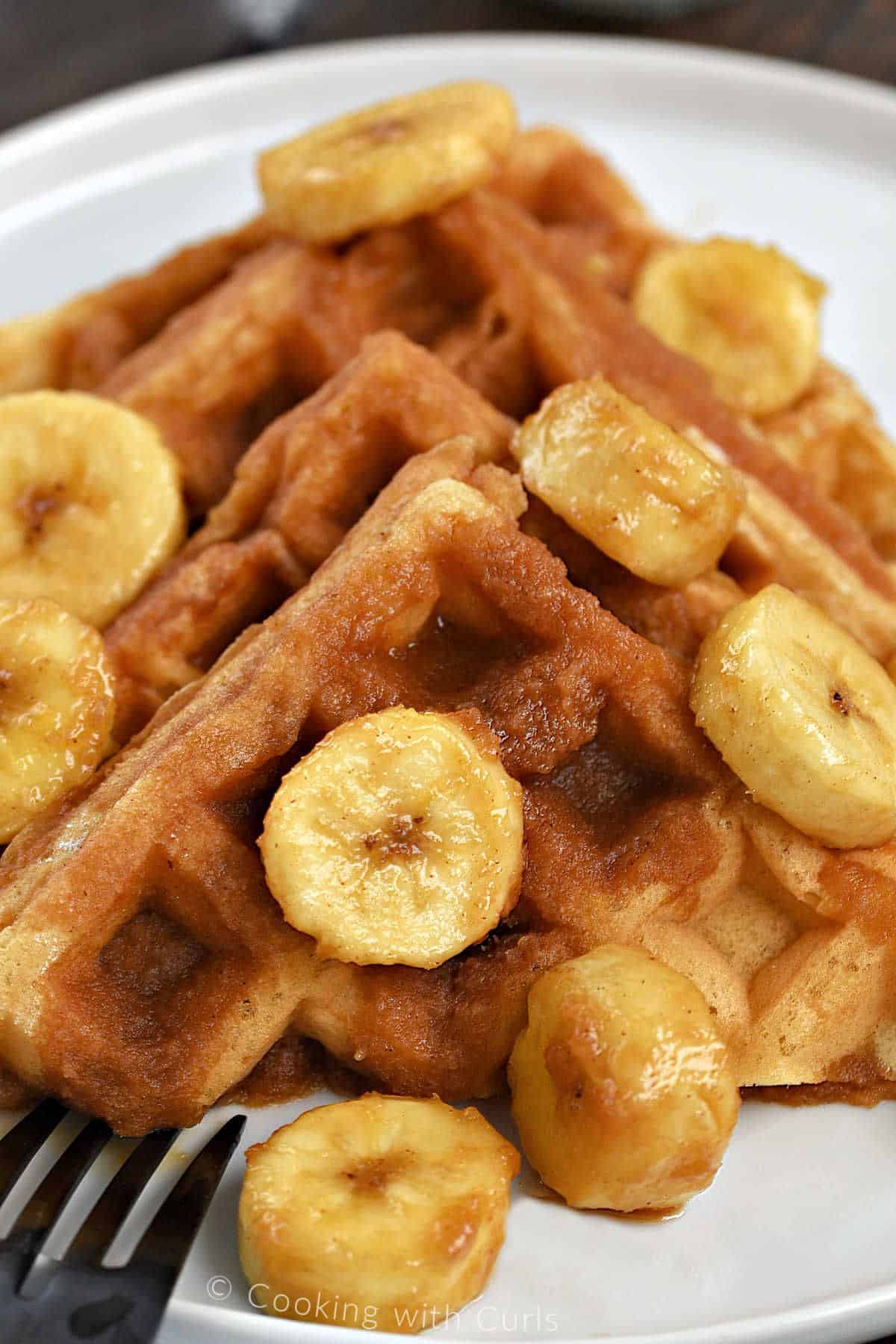 Four diagonal halves of Belgian waffles topped with Bananas Foster on a small plate. 