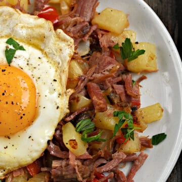 Fried egg topped corned beef hash on a plate.