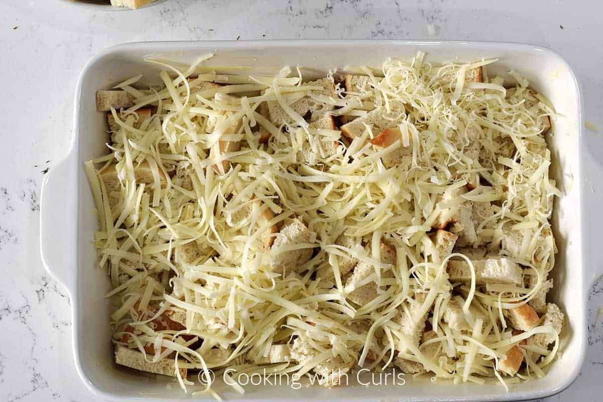 Grated cheese sprinkled over bread cubes in a buttered baking dish. 