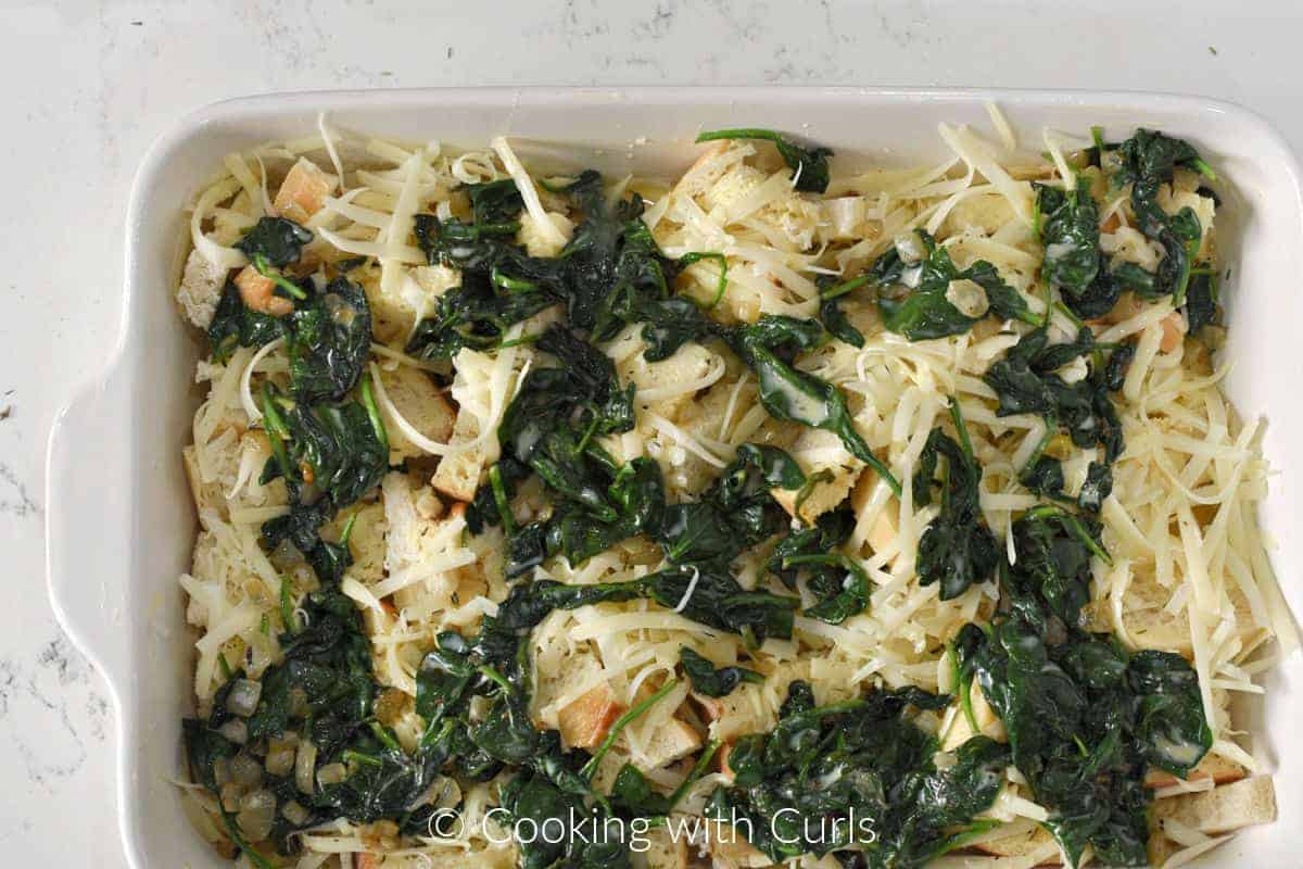 Half of the spinach and egg mixture poured over the bread cubes and shredded cheese in a baking dish. 
