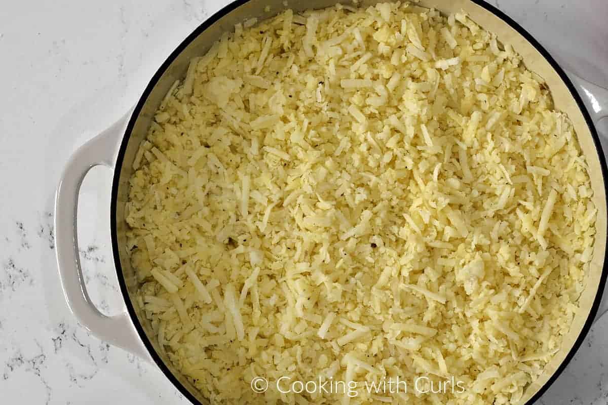 Hash browns spread out in a large skillet. 