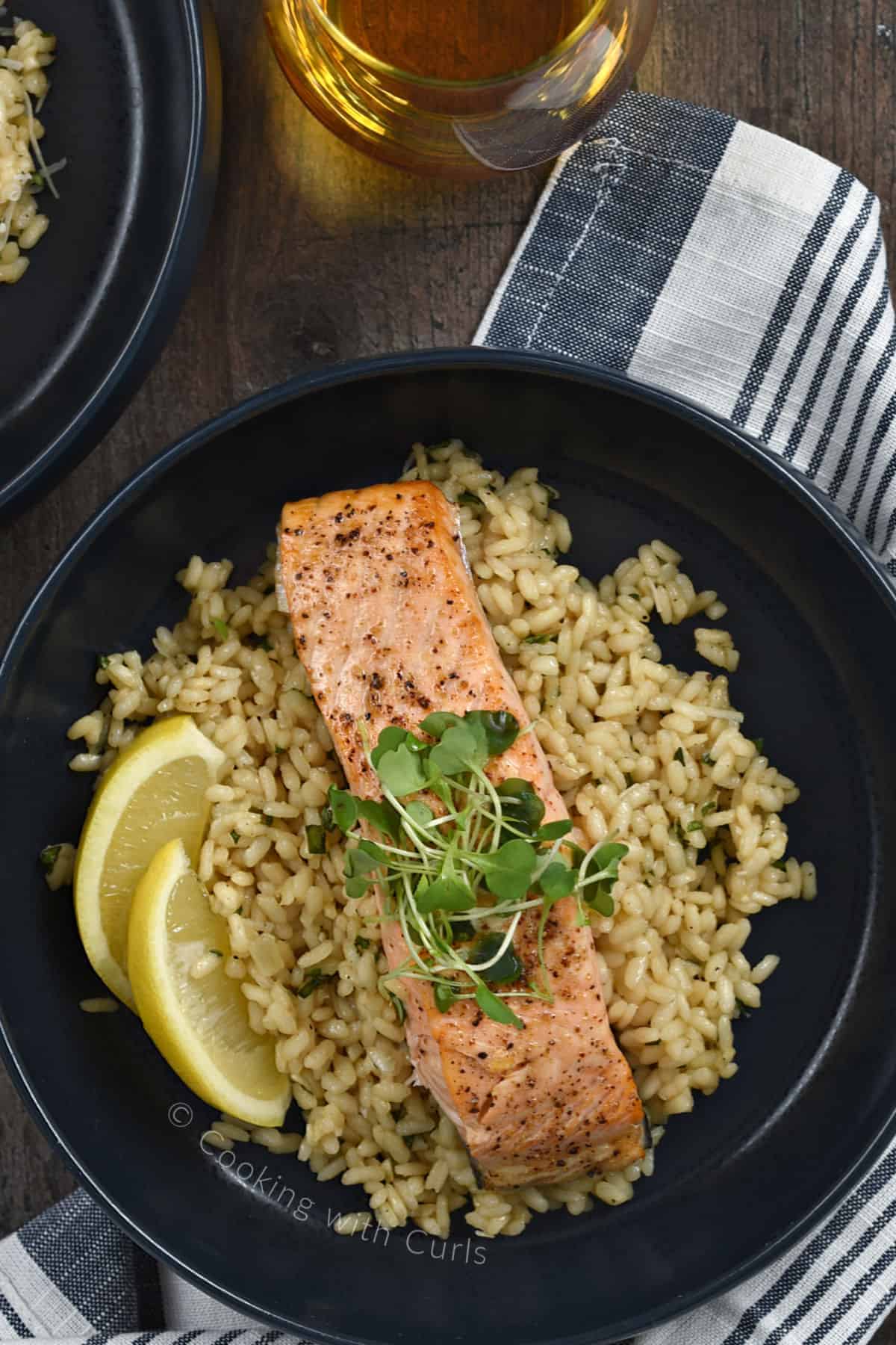 Looking down on an air fryer salmon filet on a bed of risotto with two lemon wedges on the side. of the plate. 