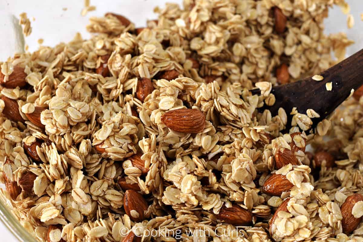 Oats, almonds, oil and honey mixed together in a large bowl with a wooden spoon. 