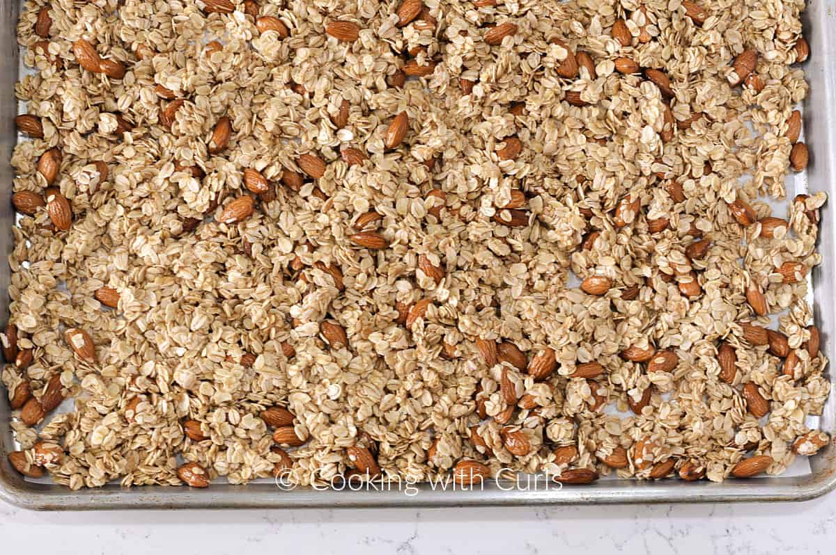 Raw vanilla almond granola spread out on a baking sheet. 