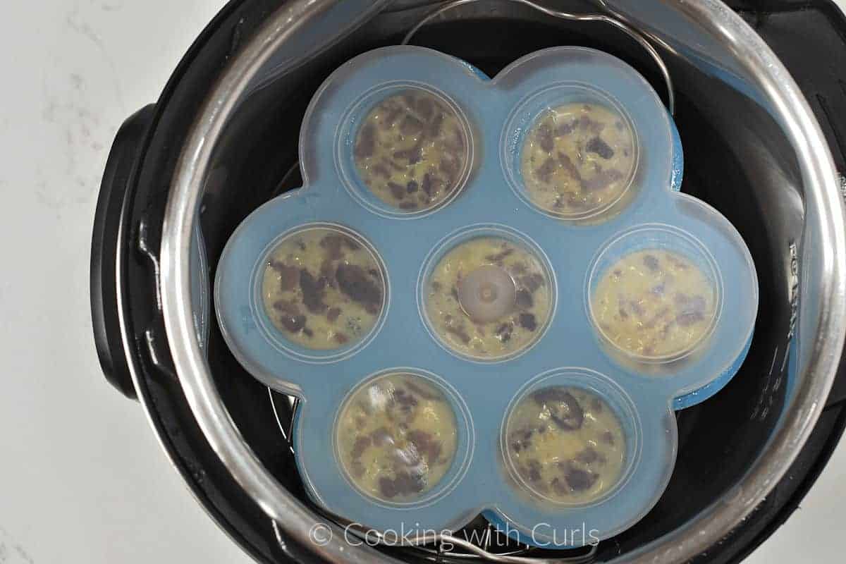 Silicone mold filled with egg bite mixture topped with a clear lid and sitting in an Instant Pot. 