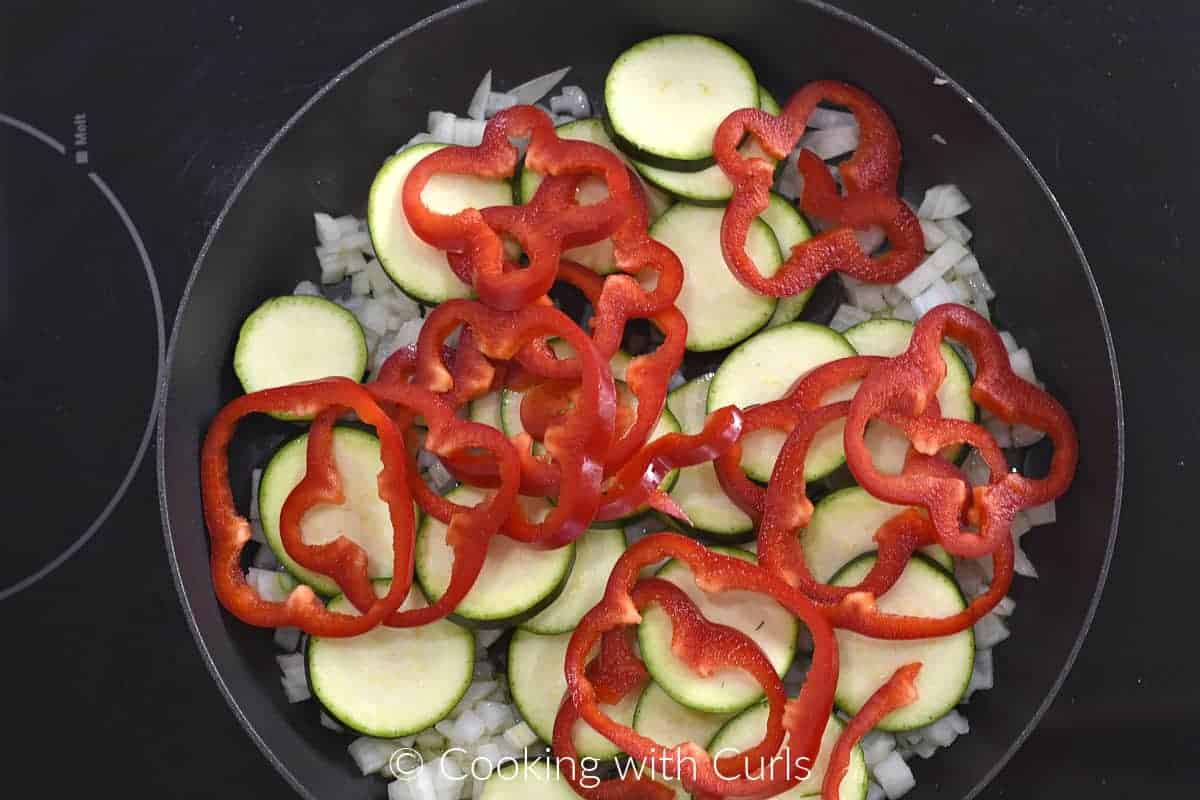 Sliced zucchini, red bell pepper rings and diced onions in a small skillet. 