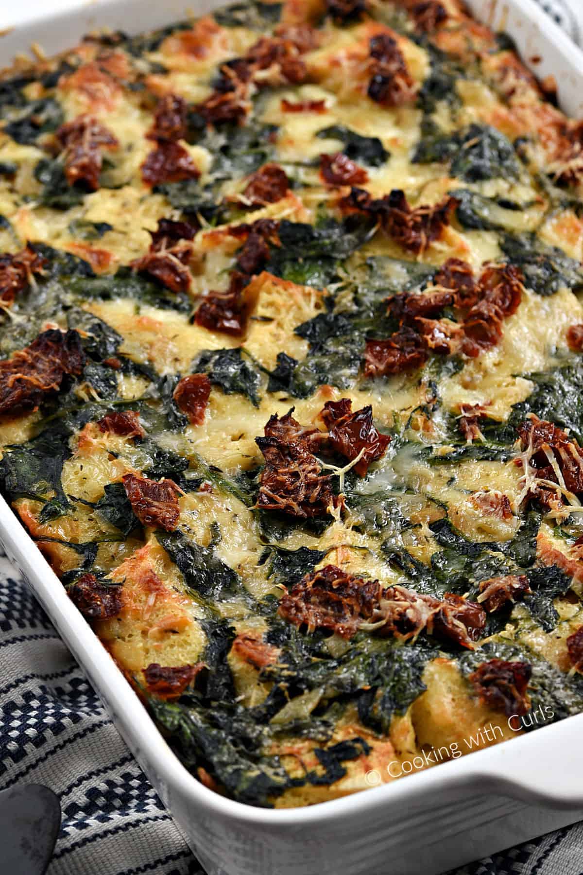 Sourdough Breakfast Strata with spinach and sun-dried tomatoes in a baking dish. 