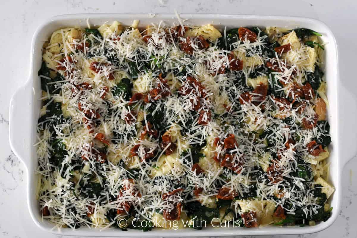 Sourdough bread cubes, spinach and egg mixture topped with grated parmesan cheese in a baking dish. 