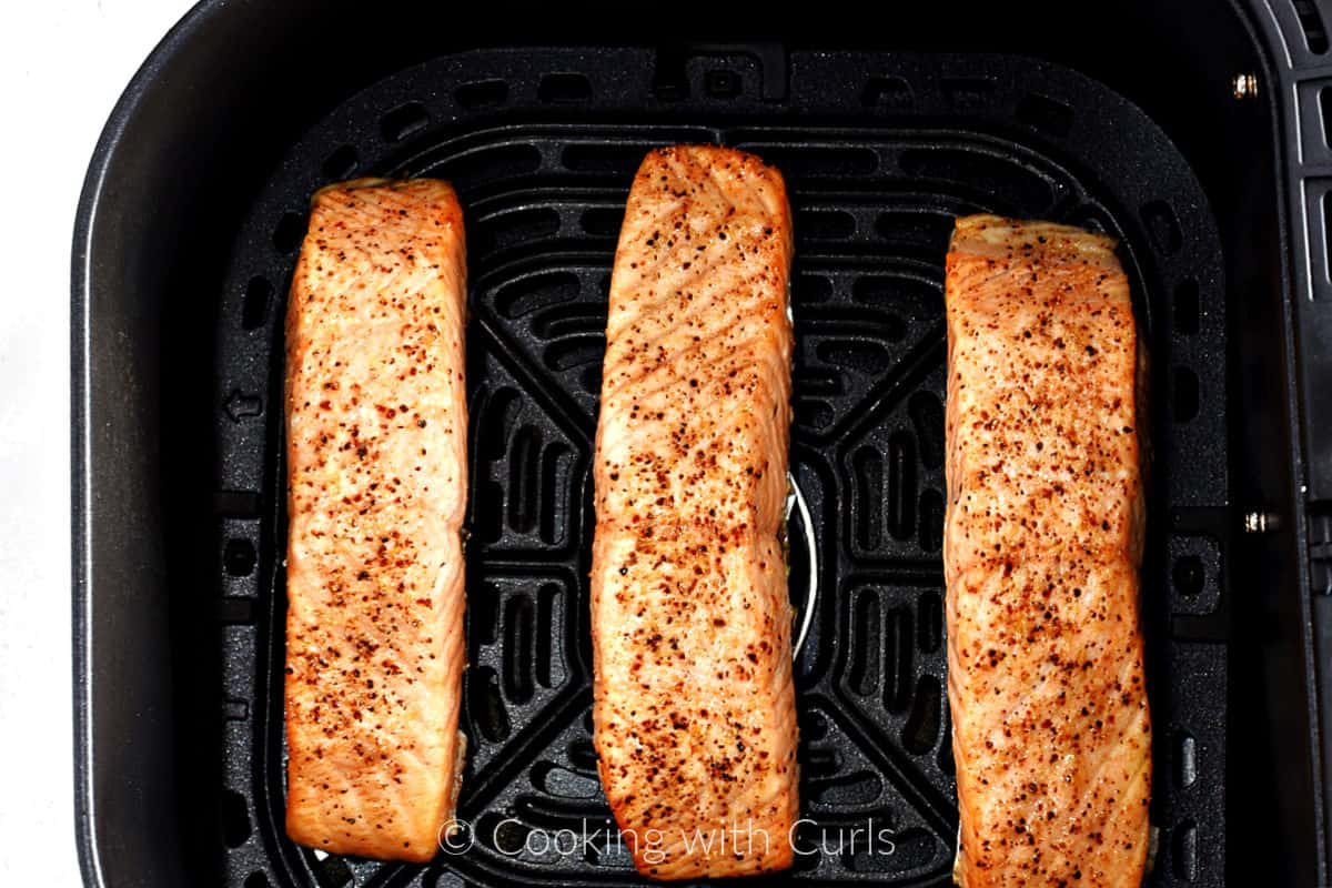 Three cooked, center-cut salmon filets in an air fryer basket. 