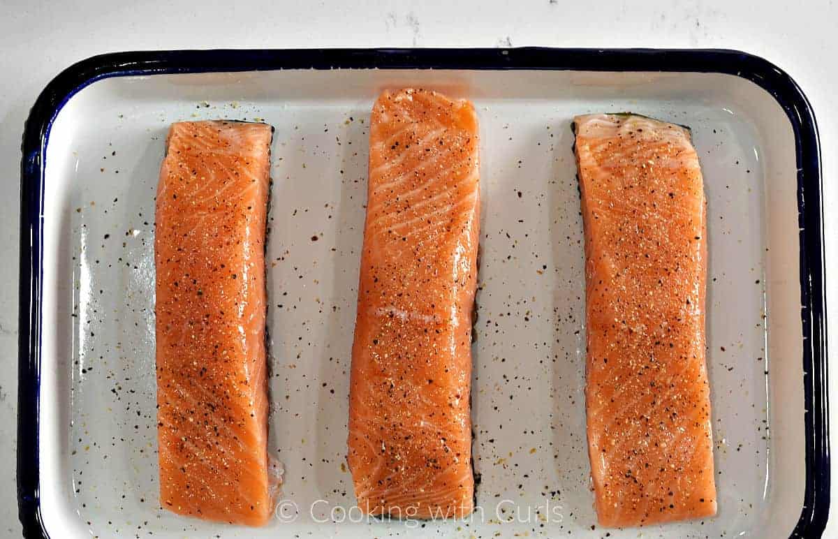 Three salmon filets on a platter sprinkled with garlic pepper salt. 