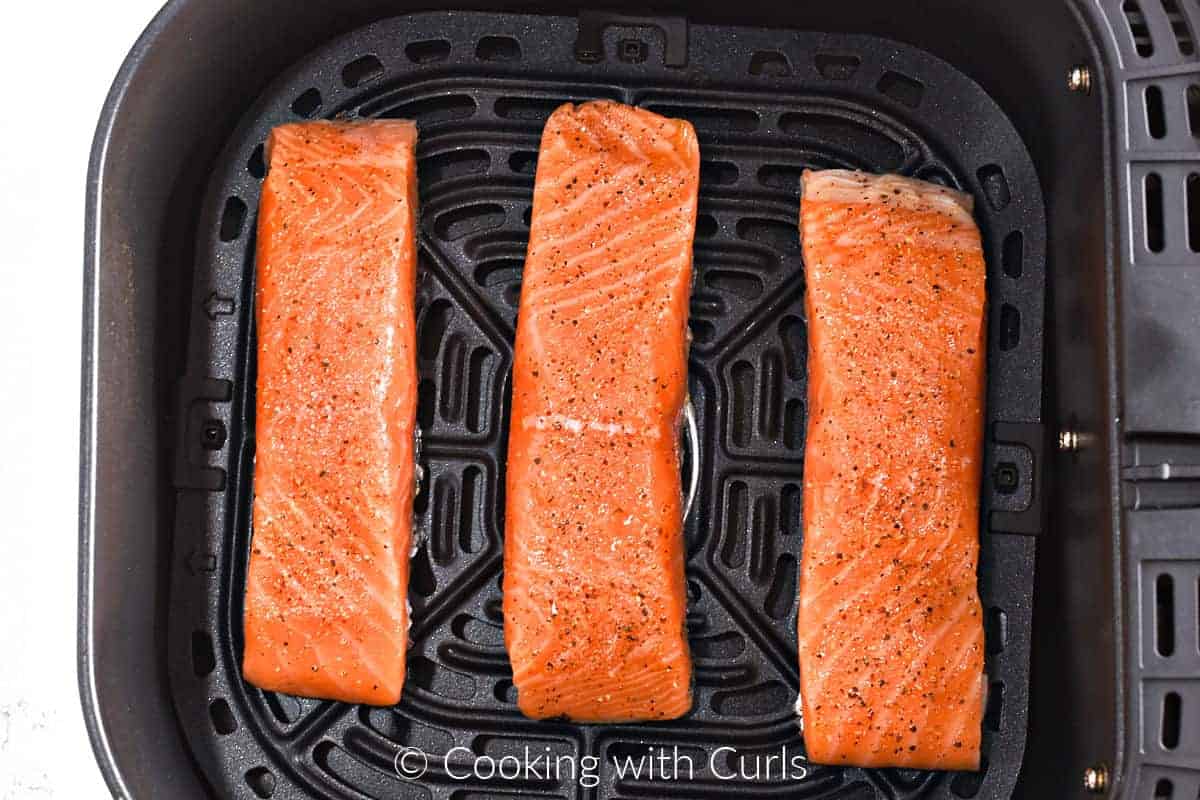 Three salmon filets skin-side down in an air fryer basket. 