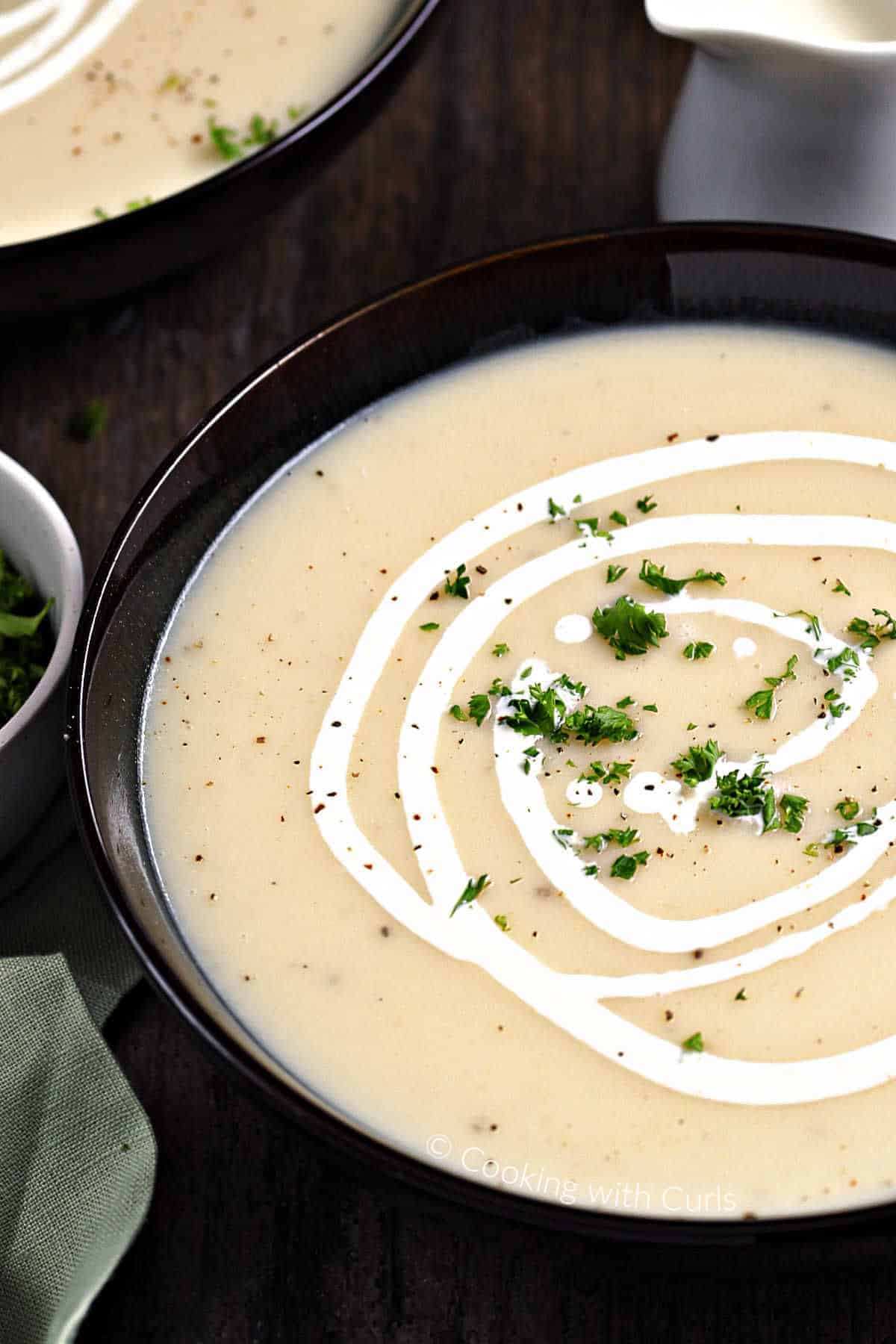 Traditional Irish Potato Leek Soup in a dark bowl drizzled with cream and sprinkled with minced parsley.