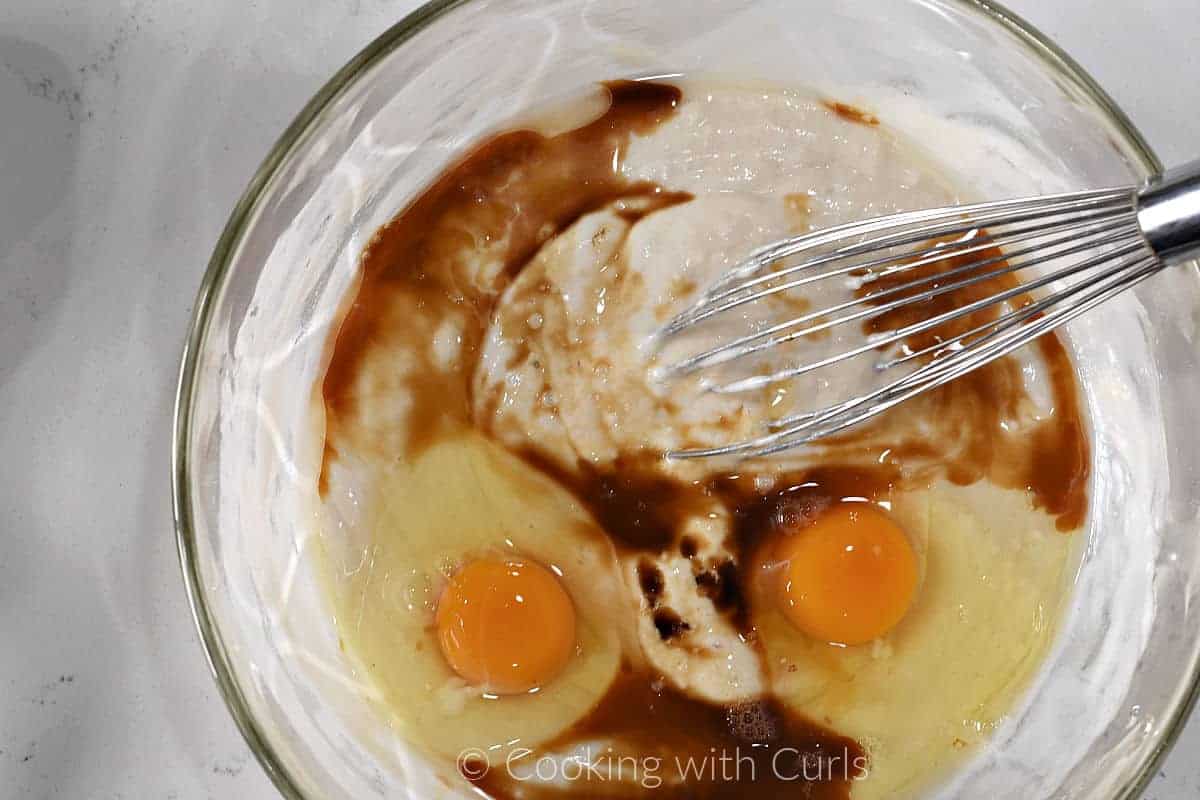 Waffle batter, two eggs and vanilla extract in a large bowl with a wire whisk. 