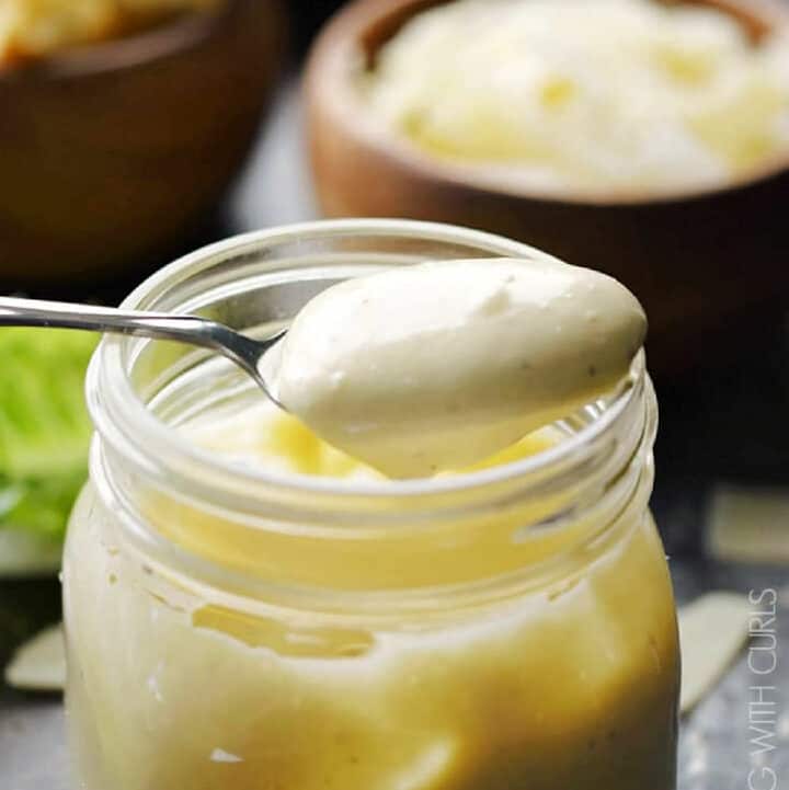 Homemade Caesar salad dressing in a glass jar with a tablespoon of dressing hovering above.