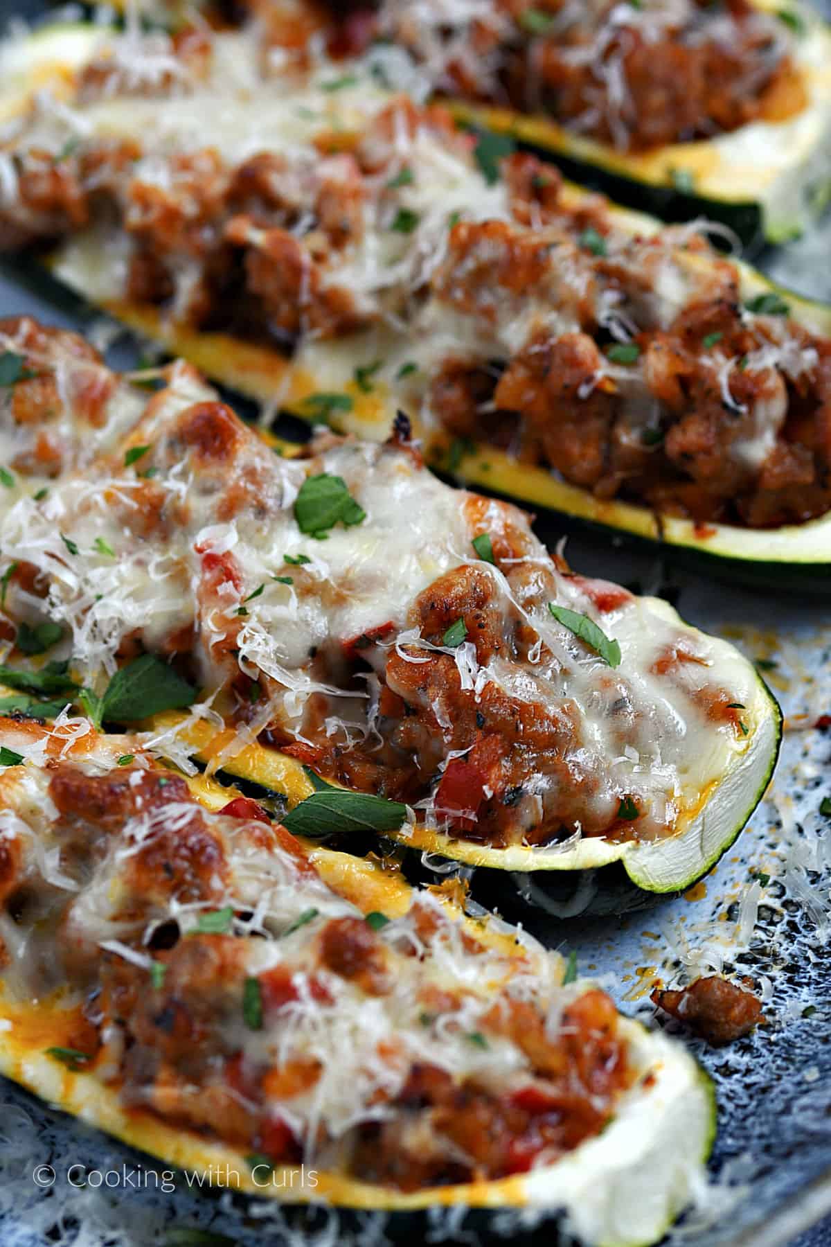 Four sausage stuffed zucchini boats topped with melted mozzarella cheese on a platter.