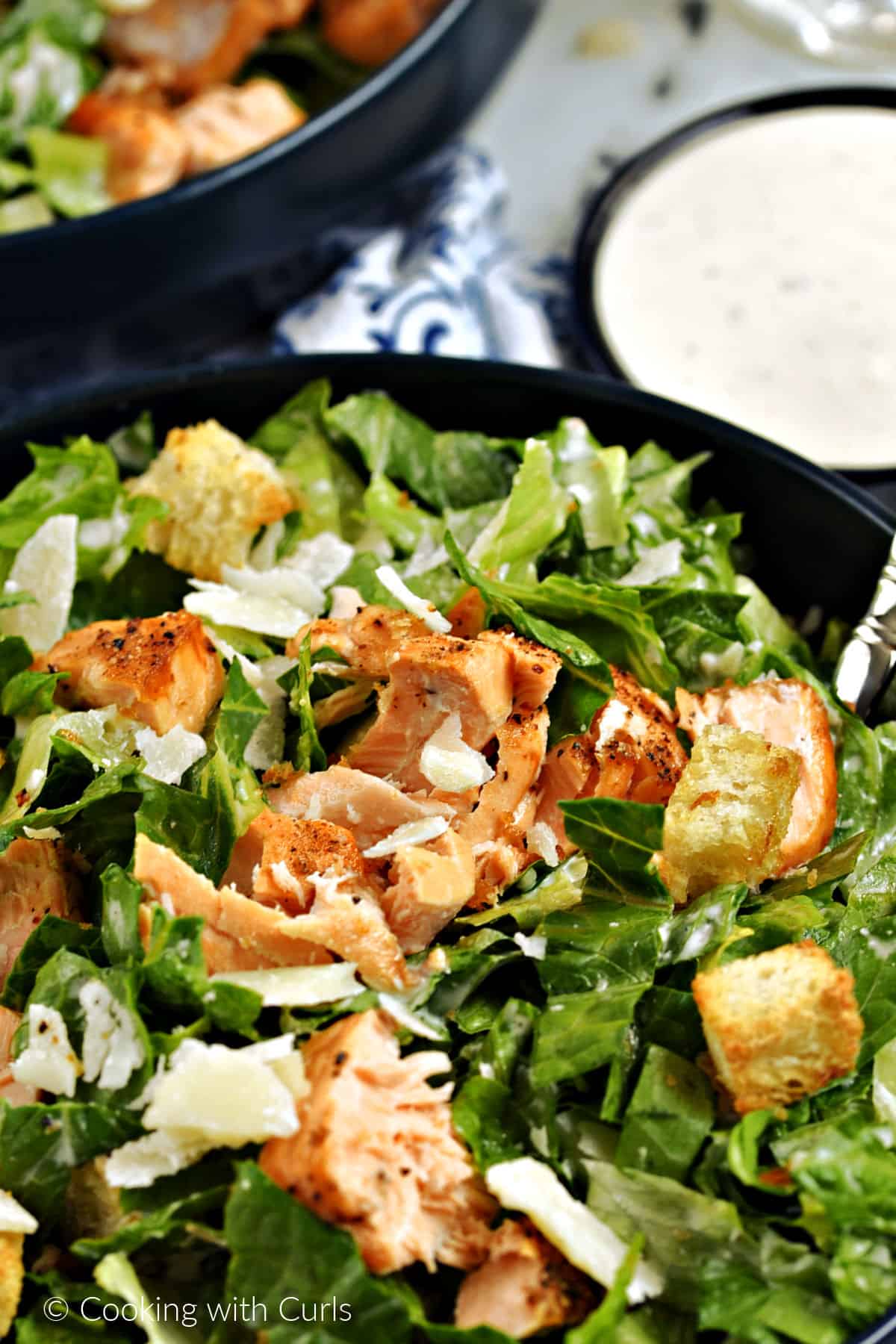 Chopped salmon on top of romaine lettuce, croutons, shaved parmesan and Caesar dressing with a small bowl of dressing on the side.