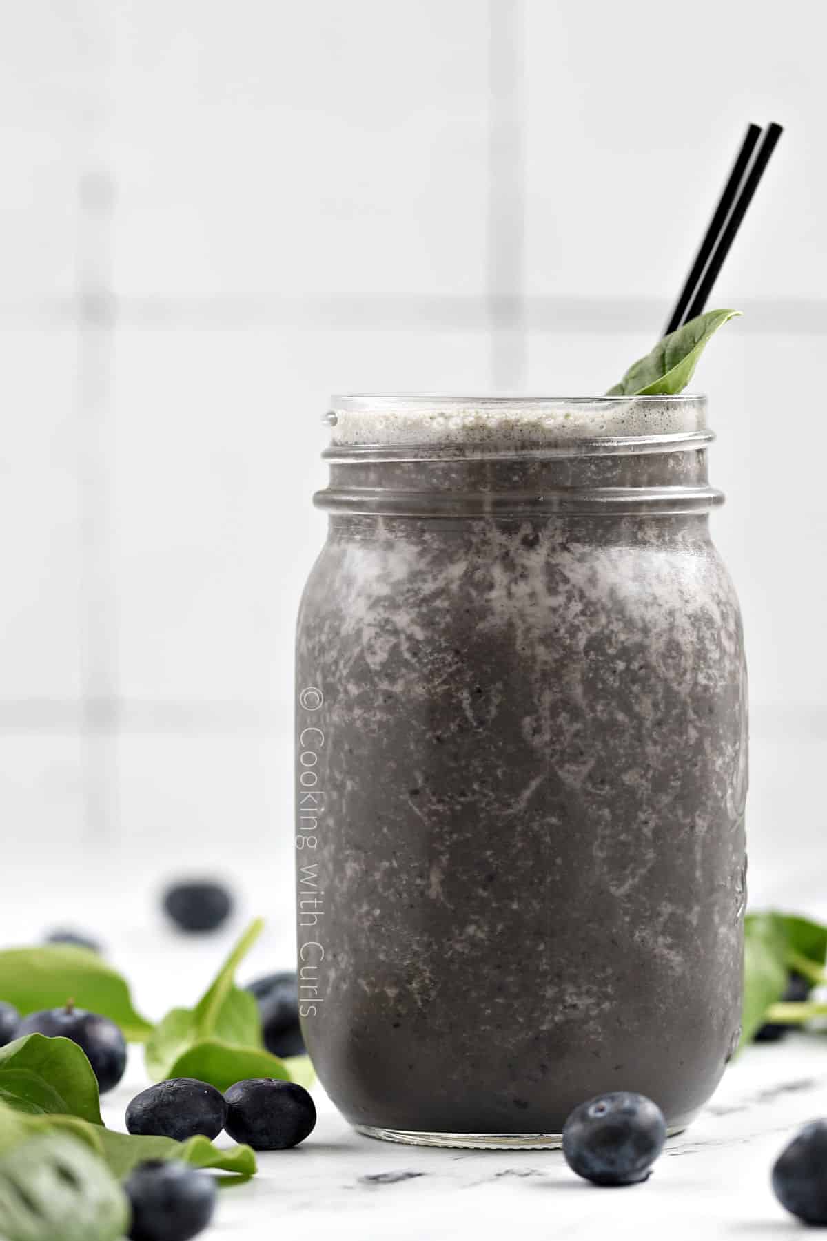 Side view of a blueberry spinach smoothie in a mason jar surrounded by fresh blueberries and spinach leaves.