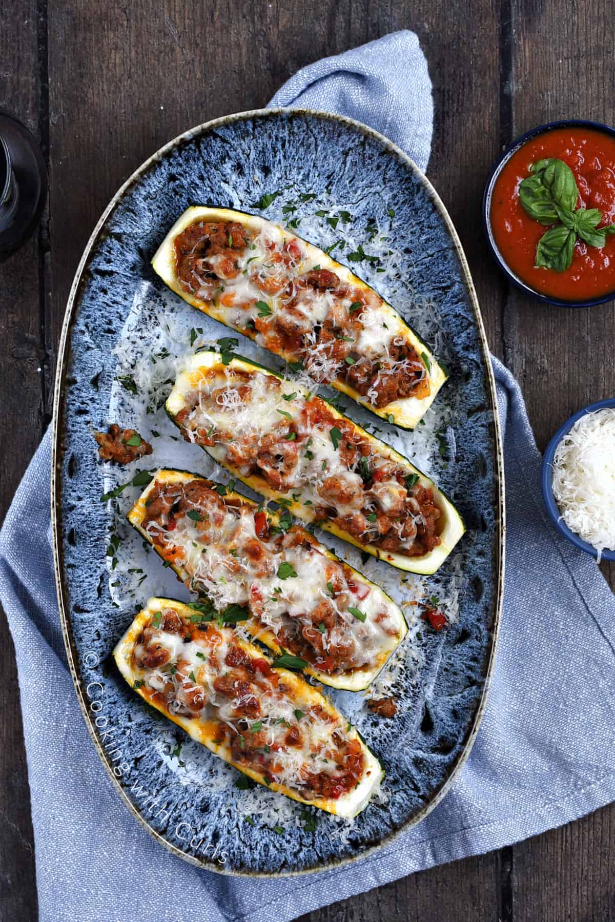 Looking down on four sausage stuffed zucchini boats topped with melted mozzarella cheese on a platter.