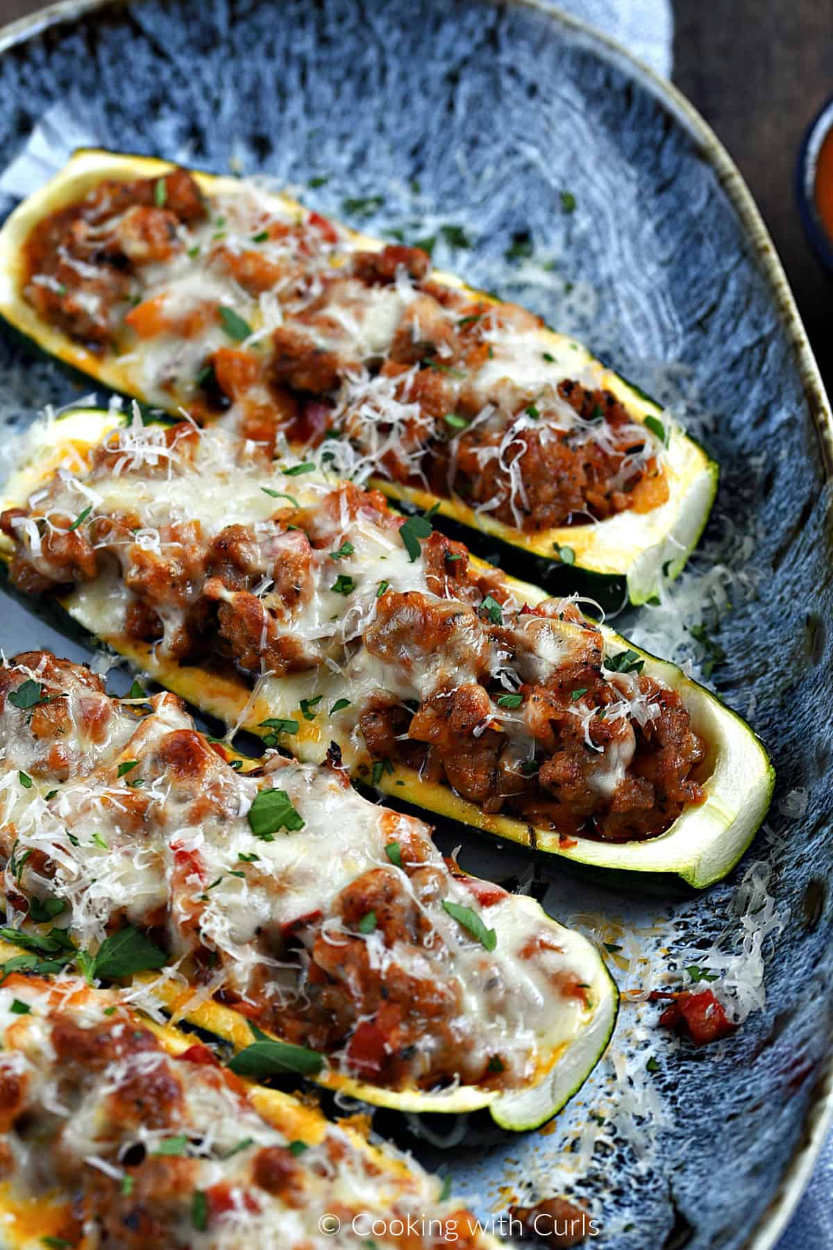 Four sausage stuffed zucchini boats topped with melted mozzarella cheese on a platter.