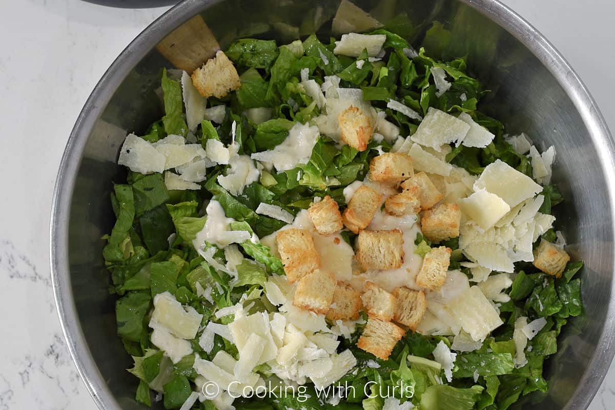 Romaine lettuce, shaved parmesan, Caesar dressing and croutons in a large bowl. 
