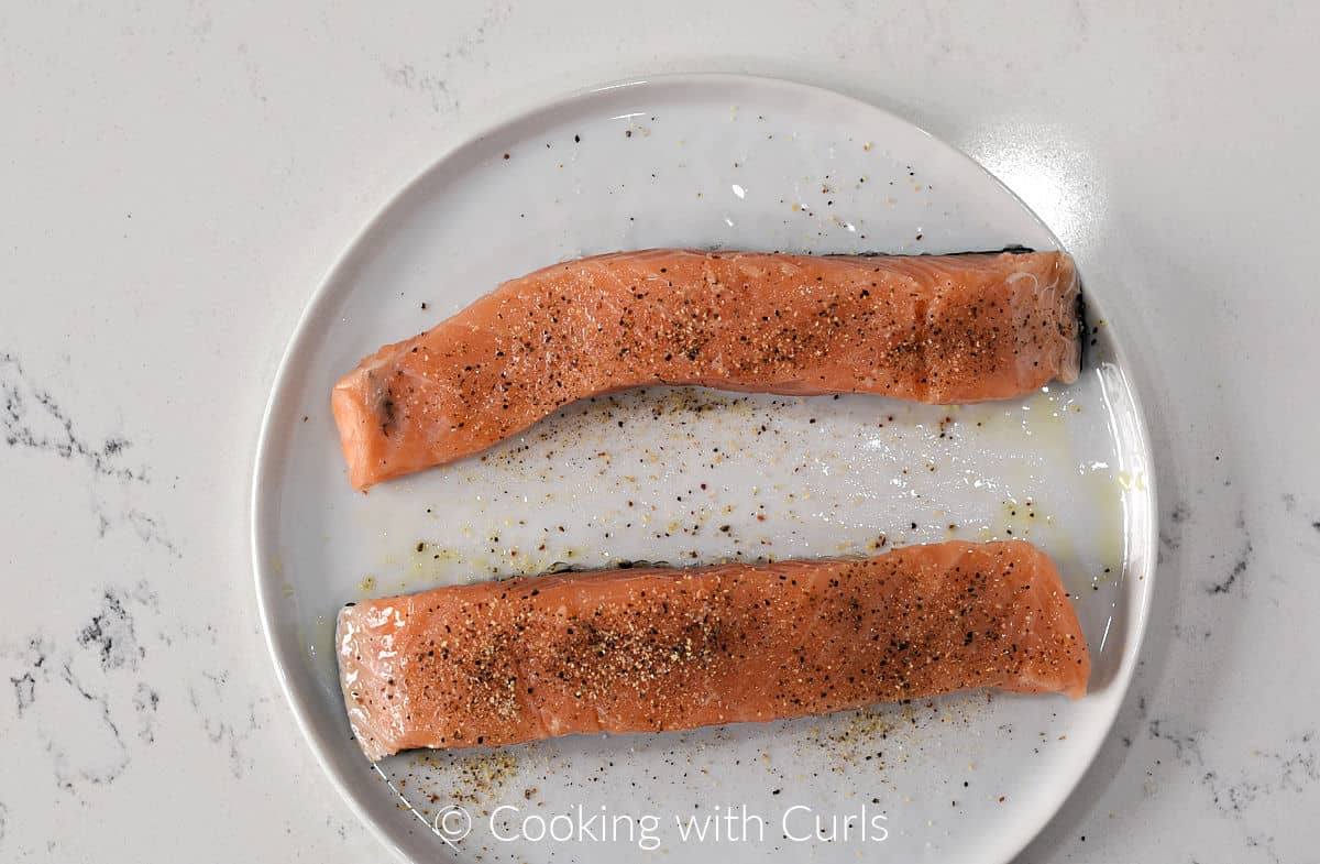 Two salmon fillets seasoned with oil and garlic pepper on a small plate. 