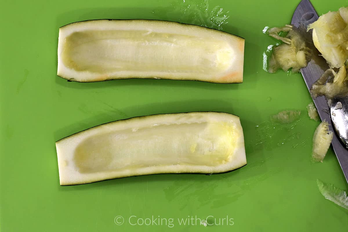 Two zucchini halves with the center scooped out sitting on a cutting board. 
