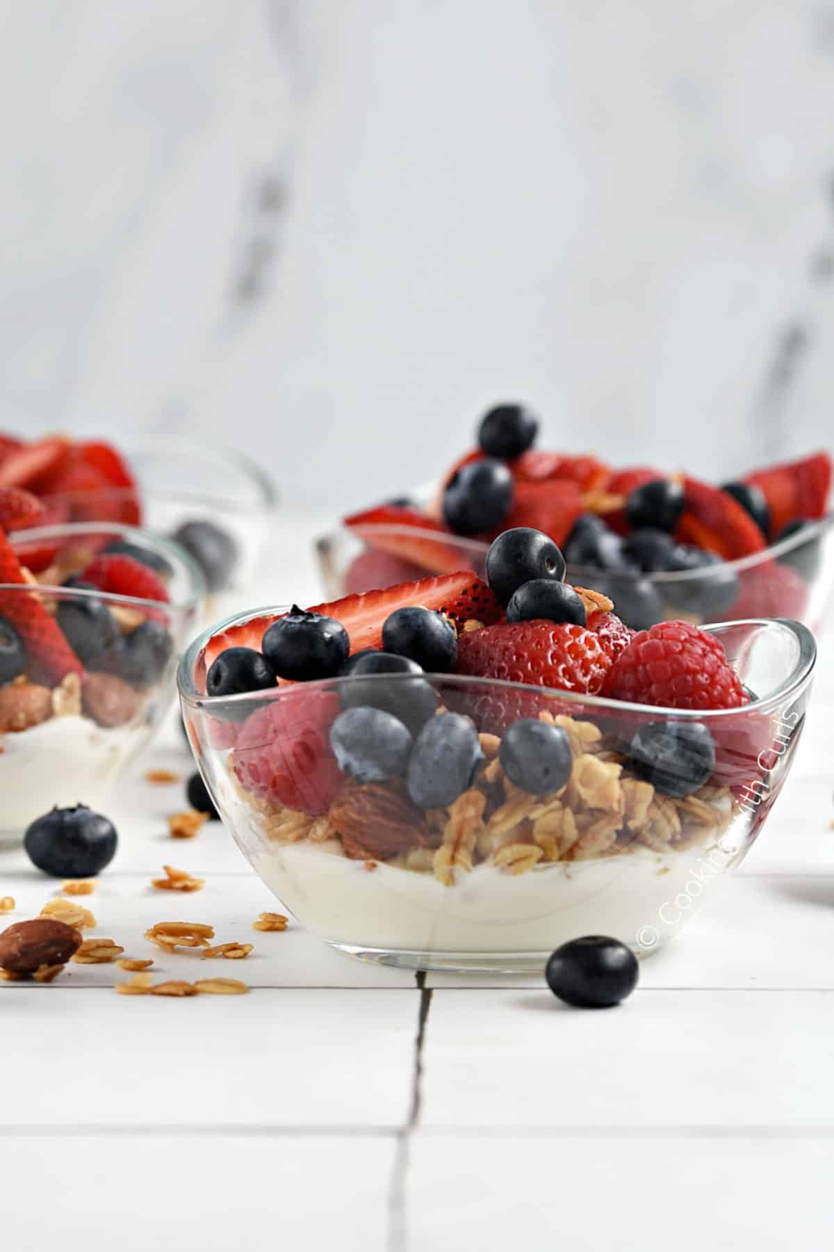 Greek yogurt, granola, fresh raspberries, strawberries and blueberries layered in small glass bowls.