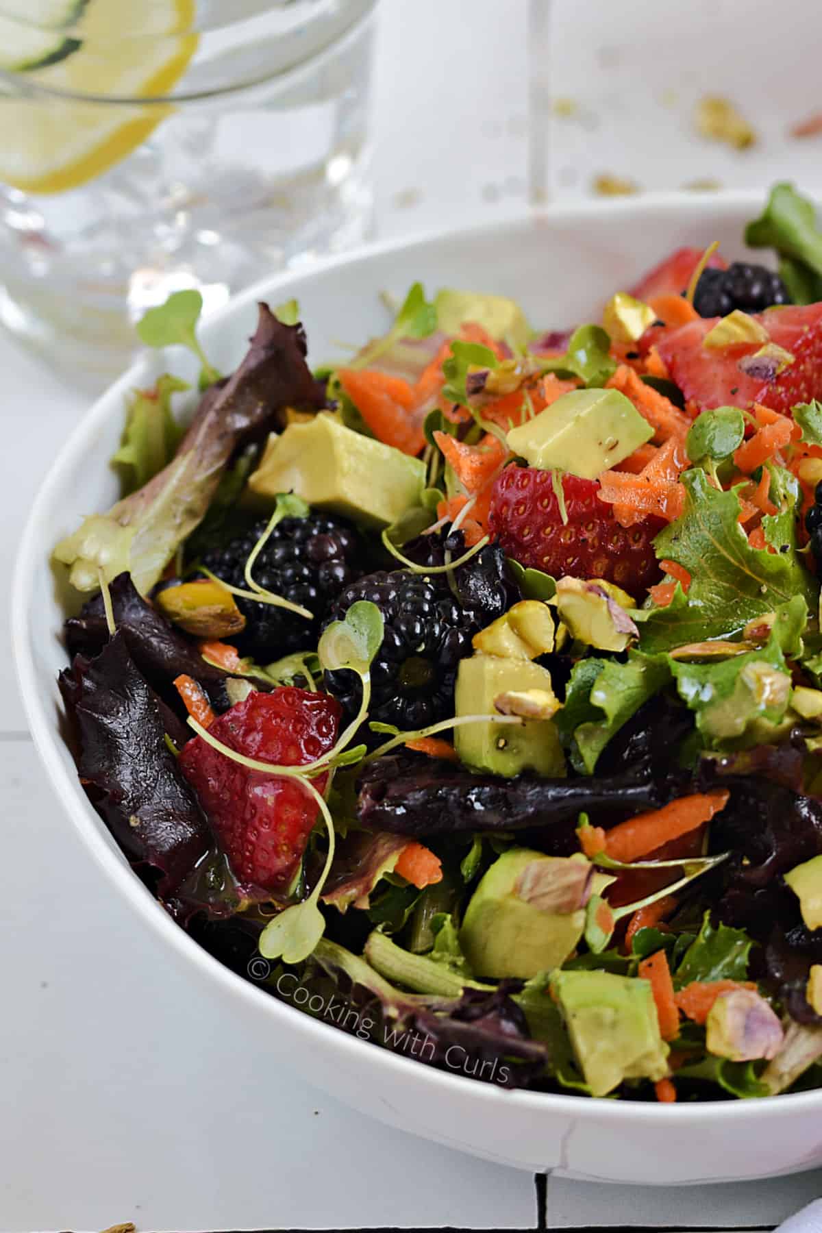 A big bowl of mixed greens, berries, avocado chunks, and pistachios. 