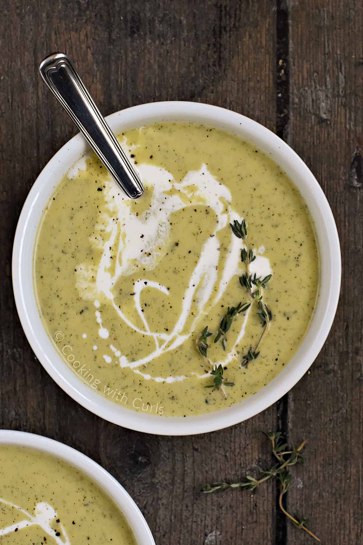 Looking down on a bowl of creamy zucchini soup swirled with cream and topped with fresh thyme sprigs.