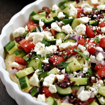Diced cucumber, tomato, olives and crumbled cheese over a base of hummus in a ceramic tart pan.