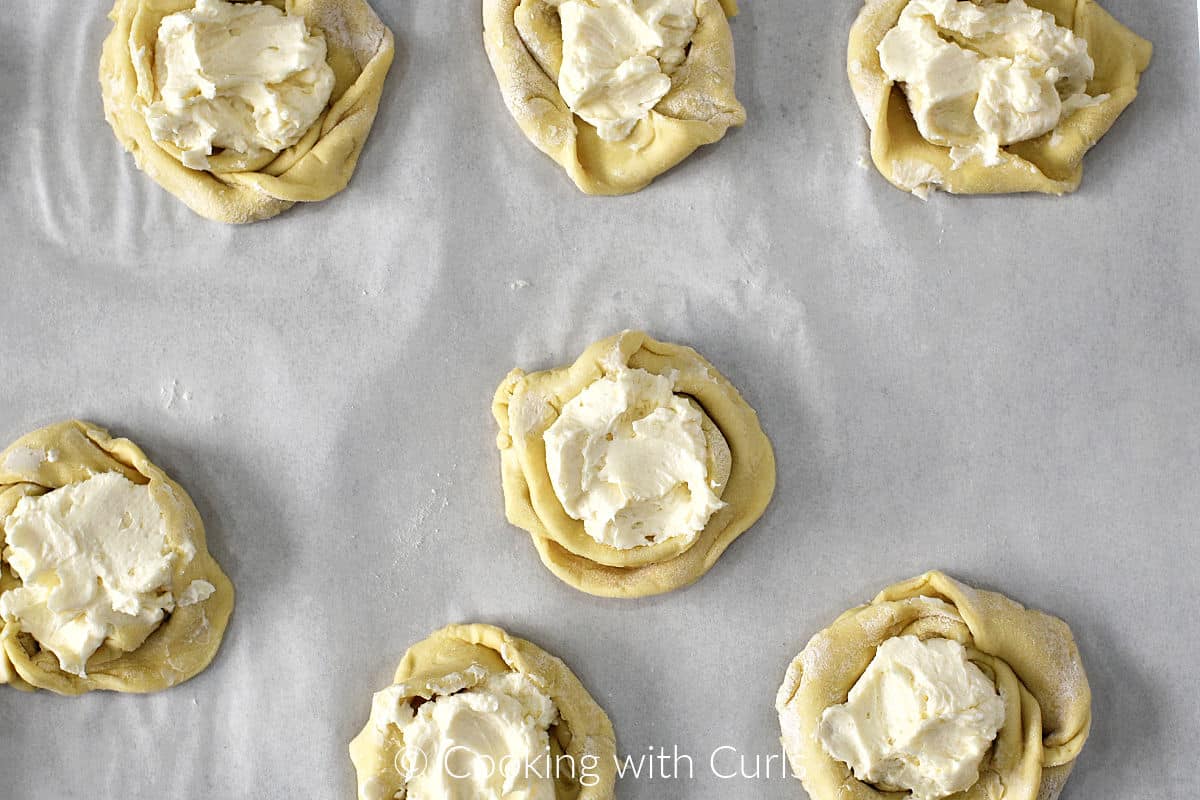 Seven puff pastry swirls filled with cream cheese filling on parchment paper. 