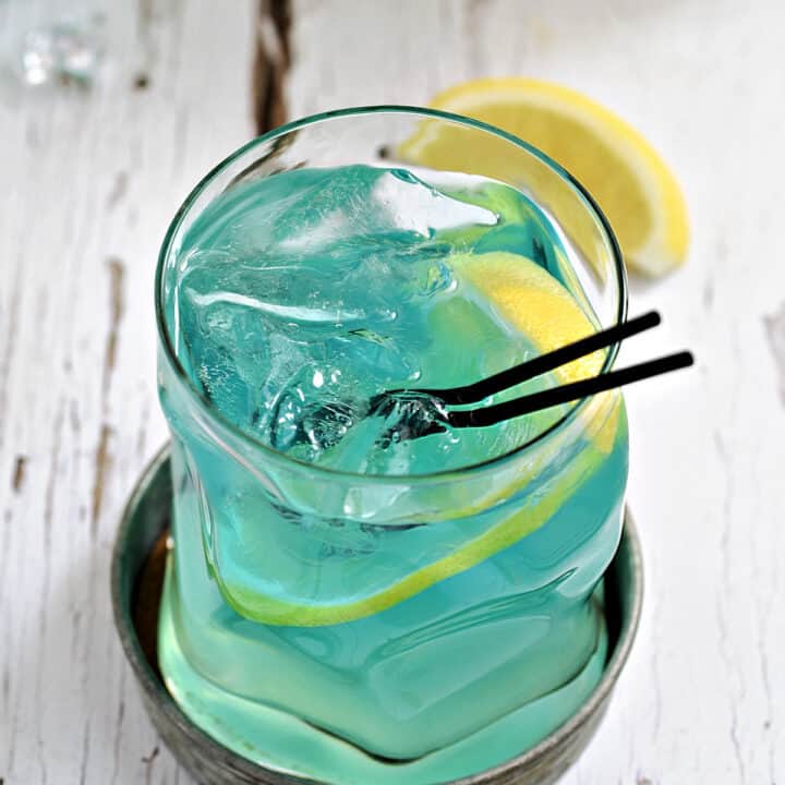 Bright blue cocktail with lemon slices and black straws.