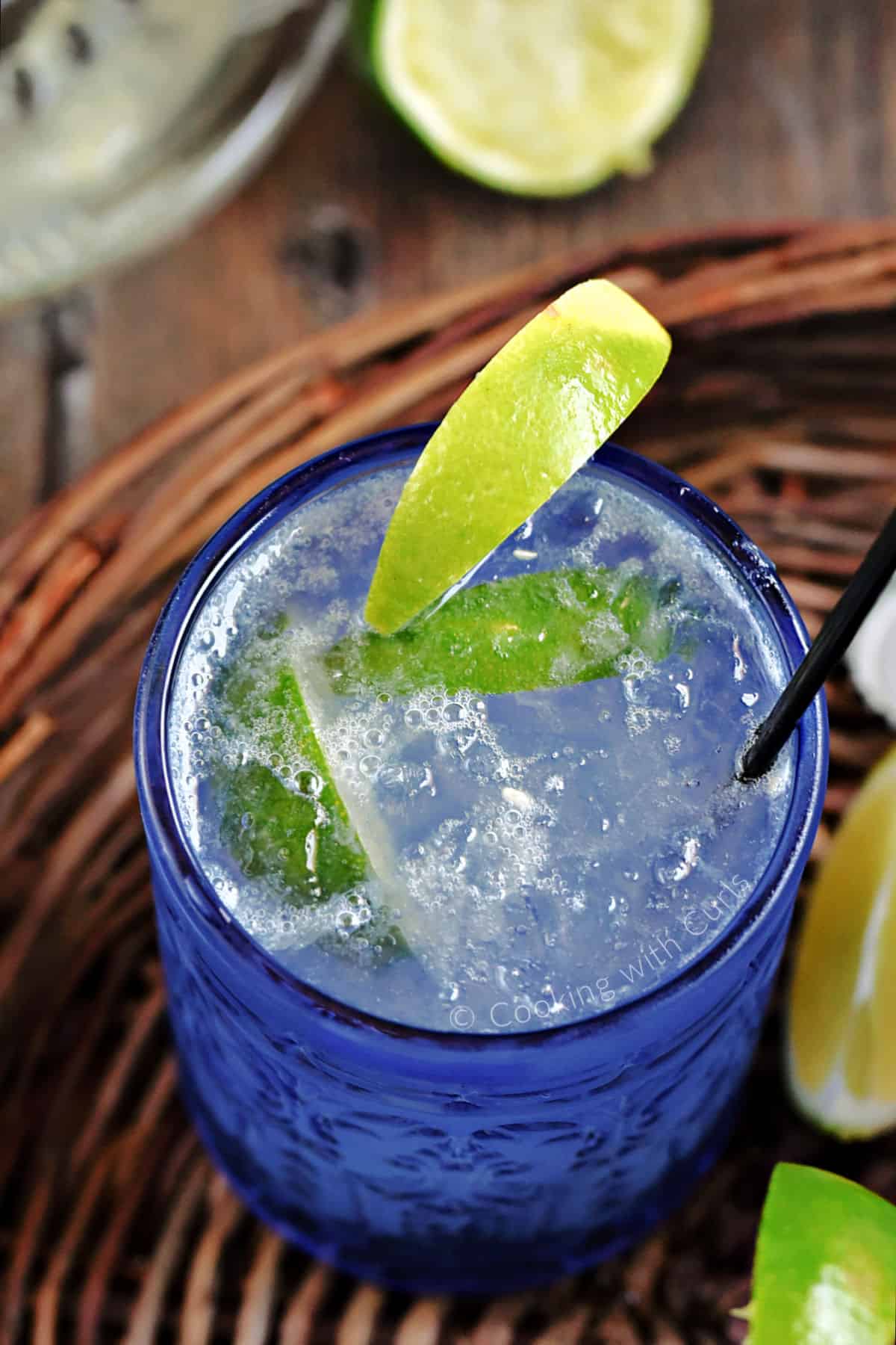 Looking down on a blue glass filled with a bubbly clear drink with lime wedge garnish.