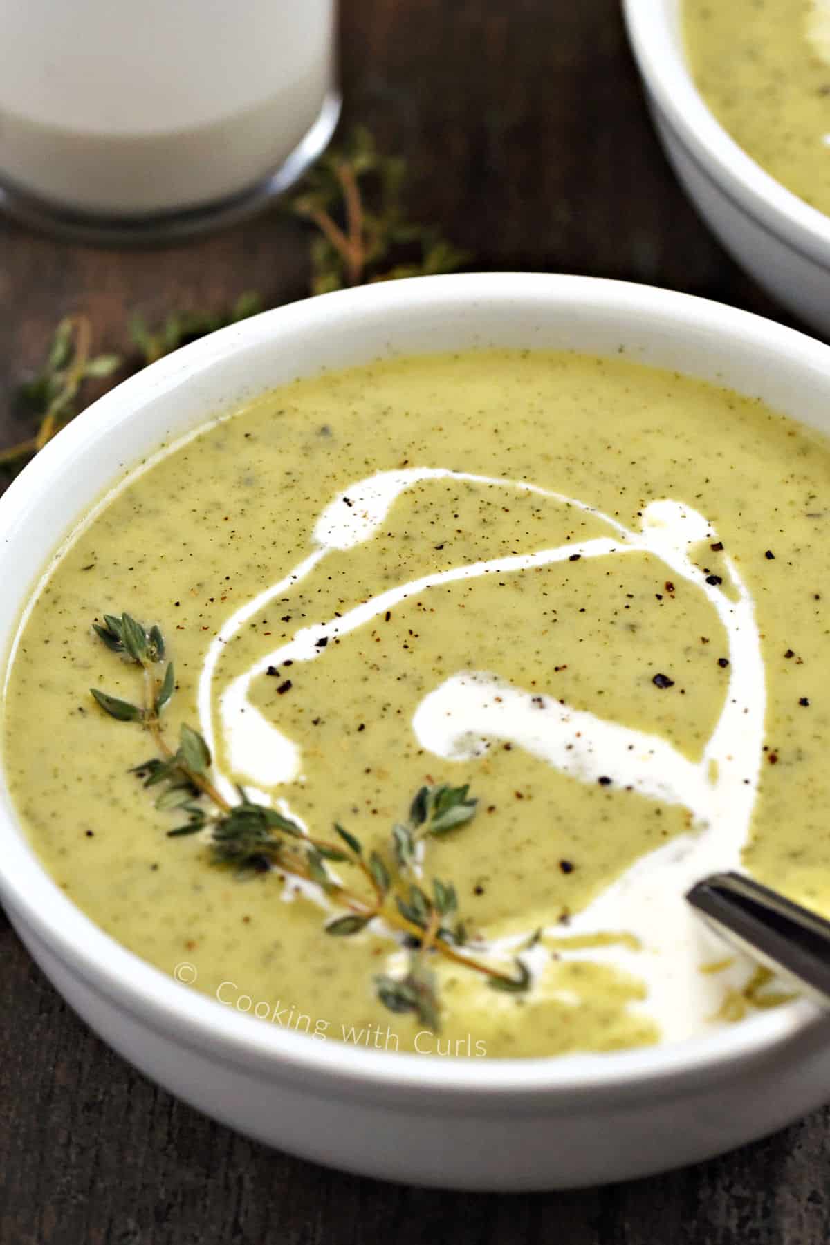 A bowl of creamy zucchini soup swirled with cream and topped with fresh thyme sprigs.